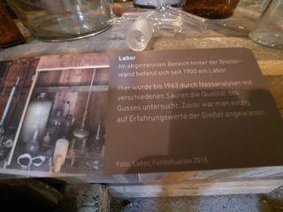 Schild mit Text über ein Labor, das bis 1963 zur Gussanalyse genutzt wurde, und einem Foto des Labors mit Glasgeräten.