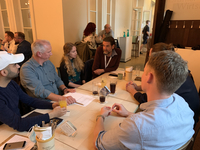 Eine diverse Gruppe von Menschen unterhält sich an einem Tisch mit Getränken und Papieren in einem Restaurant oder Besprechungsraum.