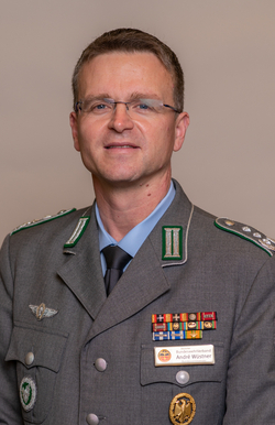 Porträt von André Wüstner, der eine deutsche Militäruniform mit Brille, Orden und Abzeichen trägt und in die Kamera lächelt.