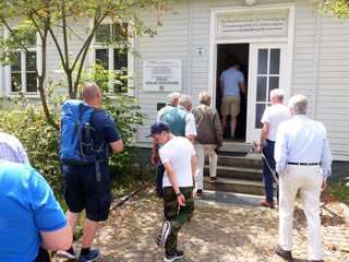 Eine Gruppe Menschen, darunter ein Junge, steht vor dem weißen Holzgebäude "Wiege der Bundeswehr".