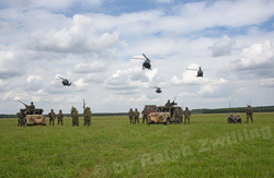 Helikopter fliegen über Soldaten und Militärfahrzeuge auf einem grünen Feld während einer Militärübung.
