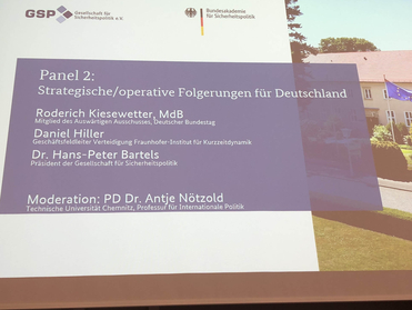 Präsentationsfolie für 'Panel 2: Strategische/operative Folgerungen für Deutschland' mit Namen der Sprecher, teils ein Gebäude mit EU-Flagge zeigend.