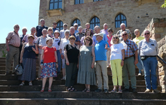 Eine große Gruppe lächelnder älterer Menschen posiert für ein Gruppenfoto auf Steinstufen vor einem historischen Gebäude.