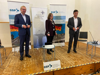Drei Sprecher auf einer Bühne vor Bannern der Gesellschaft für Sicherheitspolitik und der Deutschen Atlantischen Gesellschaft.