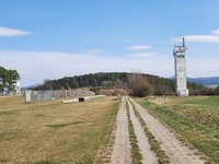 Zwei Beobachtungstürme einer historischen Gedenkstätte, mit gepflastertem Weg über Grasfeld zu bewaldetem Hügel unter blauem Himmel.