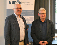 Zwei lächelnde Männer stehen vor einem Banner der 'GSP Gesellschaft für Sicherheitspolitik'.