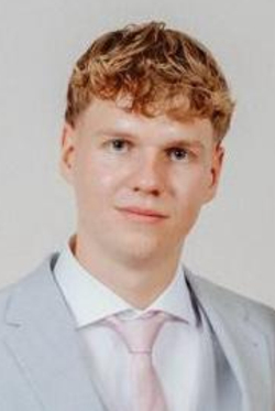 Porträt eines jungen Mannes mit blonden, lockigen Haaren, hellblauem Anzug und rosa Krawatte, blickt ruhig in die Kamera.