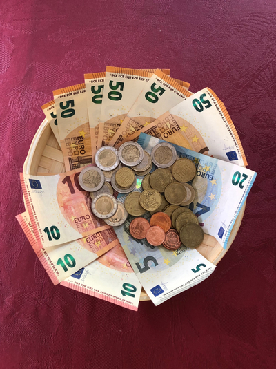 Ein Holzkorb gefüllt mit Euro-Banknoten (5, 10, 20, 50) und verschiedenen Münzen auf einer weinroten Tischdecke.