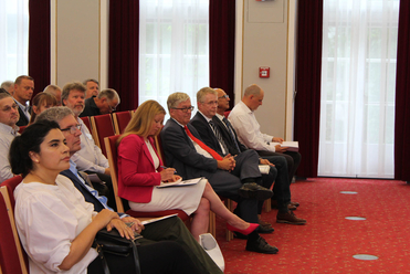 Vielfältige Gruppe von Erwachsenen sitzt in Reihen und hört aufmerksam in einem Konferenz- oder Besprechungsraum zu.