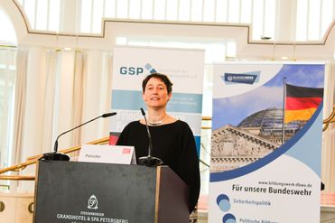 Frau Petretto spricht an einem Podium im Steigenberger Grandhotel, umgeben von Bannern der GSP und des Bildungswerks Bundeswehr.