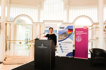 Frau am Rednerpult bei einer Konferenz, mit Bannern der Friedrich-Ebert-Stiftung und des Bundeswehr Bildungswerks.
