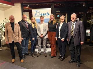 Sieben Personen, vier Männer und drei Frauen, posieren lächelnd vor einem GSP-Banner zum 70-jährigen Jubiläum.