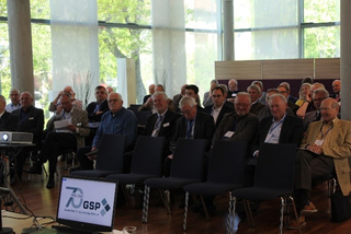Teilnehmer in hellem Konferenzraum mit Fenstern. Ein Monitor zeigt das GSP 70-Jahre-Logo während einer Präsentation.