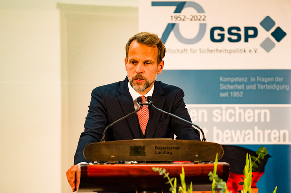 Ein Mann mit Bart im Anzug spricht an einem Pult des Bayerischen Landtags, im Hintergrund ein Banner zum 70. Jubiläum der GSP.
