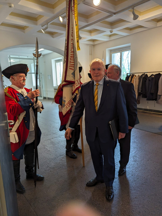 Mann im Anzug geht an historischen Wachen in roten Uniformen vorbei, die eine Pike und ein Banner halten.