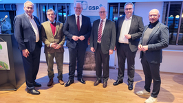 Sechs Männer in Anzügen lächeln vor einem Banner der GSP (Gesellschaft für Sicherheitspolitik e.V.).