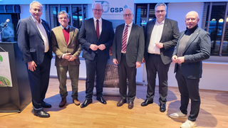 Sechs Männer in Anzügen lächeln vor einem Banner der GSP (Gesellschaft für Sicherheitspolitik e.V.).