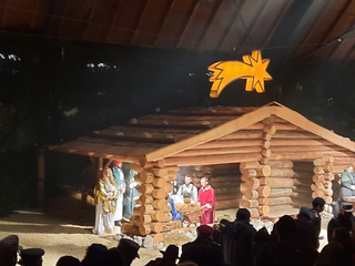 Lebendige Krippenszene bei Nacht mit Schauspielern in historischen Kostümen, die in einem Holzstall unter einem goldenen Stern auftreten.