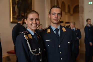 Eine lächelnde junge Frau und ein junger Mann in dunkelblauen Bundeswehr-Luftwaffe-Uniformen mit Rangabzeichen und Pilotenflügeln.
