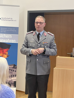 Dr. Klein, gekleidet in eine Bundeswehruniform, spricht vor einem Banner der Gesellschaft für Sicherheitspolitik e.V.
