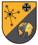 Emblem: Oben links gelb mit Netzwerkdiagramm & Eisernem Kreuz; unten rechts grau mit goldener Weltkugel, auf Europa zentriert.