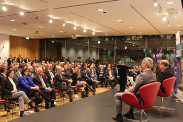 Publikum und Redner bei einer Konferenz oder Präsentation in einem modernen Raum mit Glaswänden.
