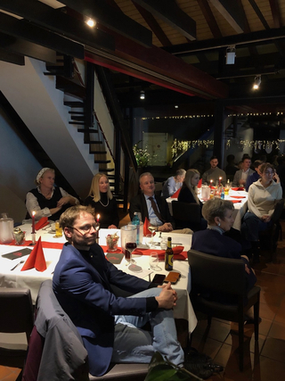 Gäste bei einem festlichen Abendessen in einem Restaurant, umgeben von gedämpftem Licht, Kerzen und roten Akzenten.