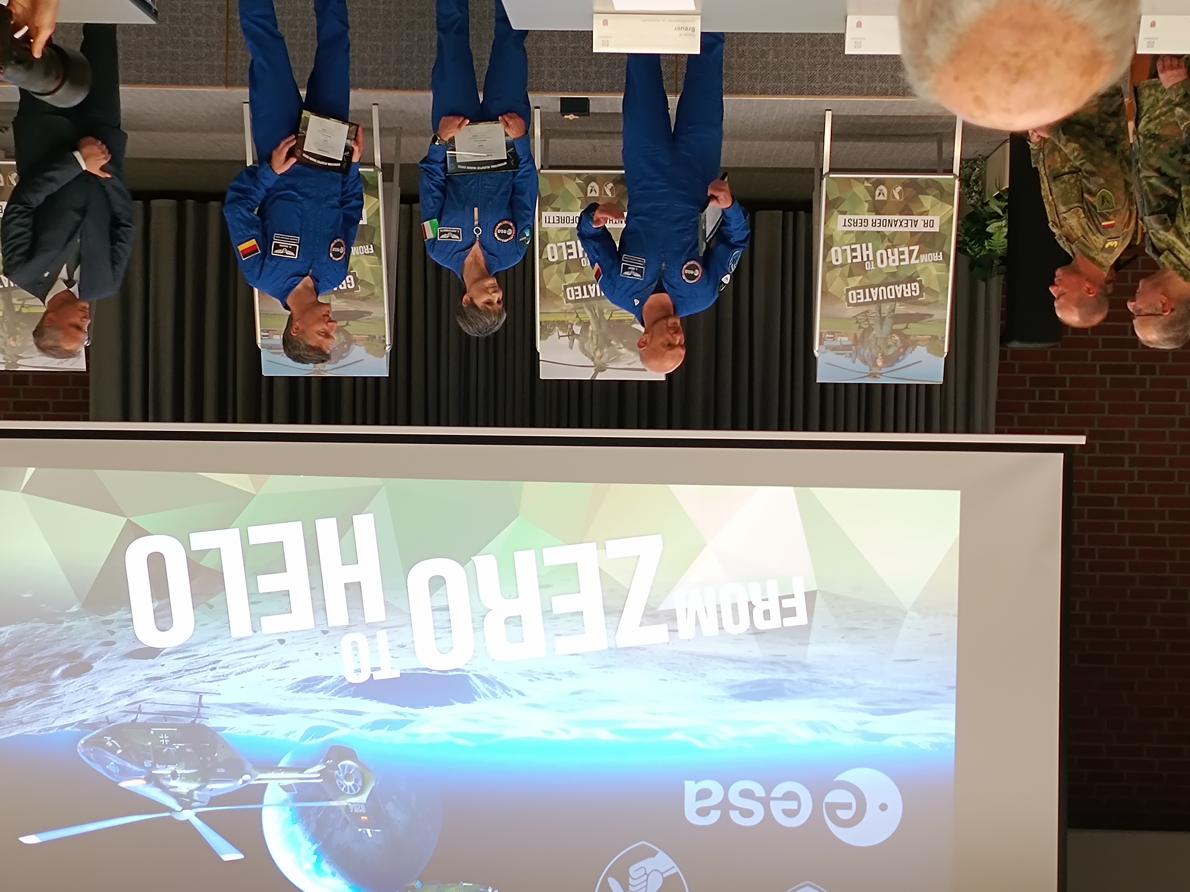 ESA-Astronauten auf der Bühne bei einem 'From Zero to Helo'-Event, mit einem Bildschirm, der einen Hubschrauber auf dem Mond zeigt.