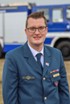 Lächelnder Mann mit Brille in blauer THW-Uniform mit Abzeichen vor einem THW-Einsatzfahrzeug.